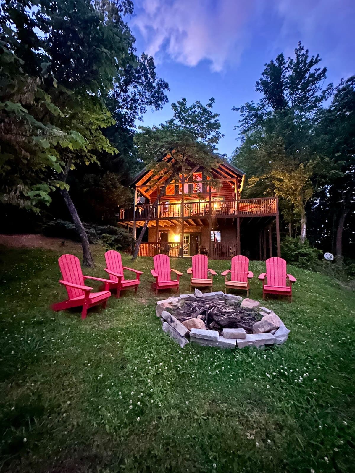 Thistle Britches cabin glowing at twilight with Adirondack chairs around fire pit